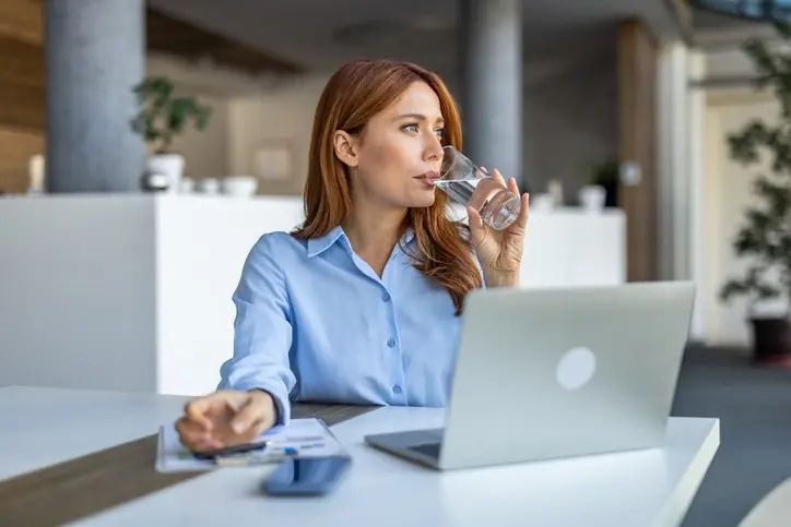 Mujer bebiendo agua y viendo su computador